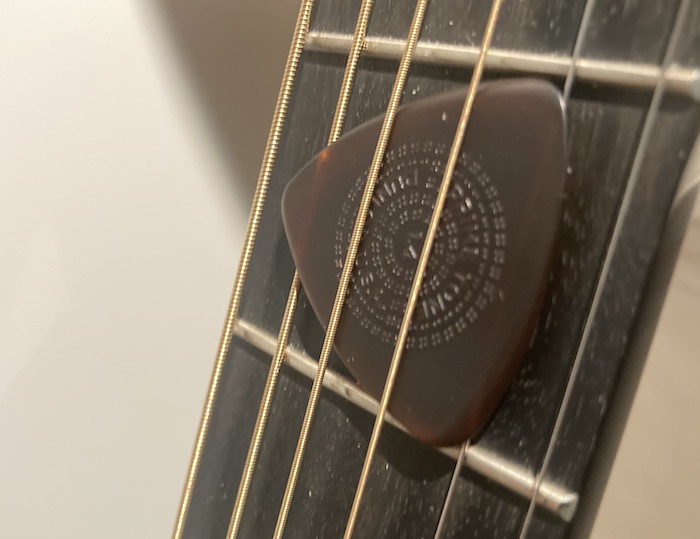 Closeup of a Jim Dunlop Primetone guitar pick wedged between the strings of a Martin D-18