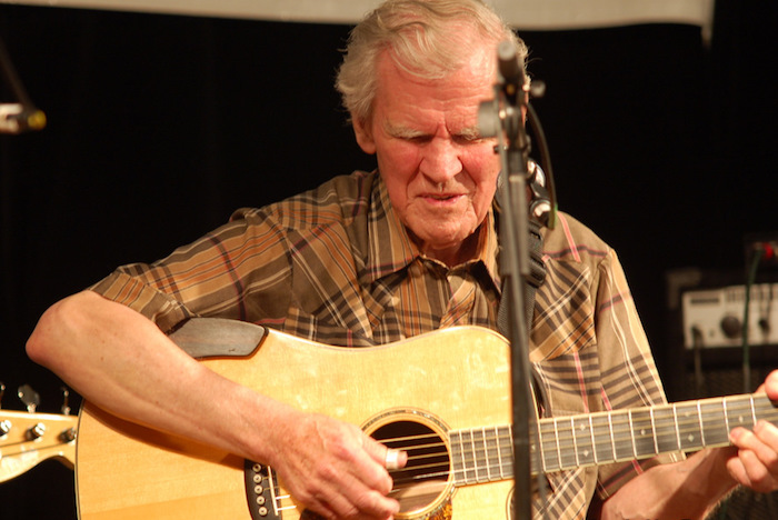 Doc Watson plays his guitar in front of a microphone