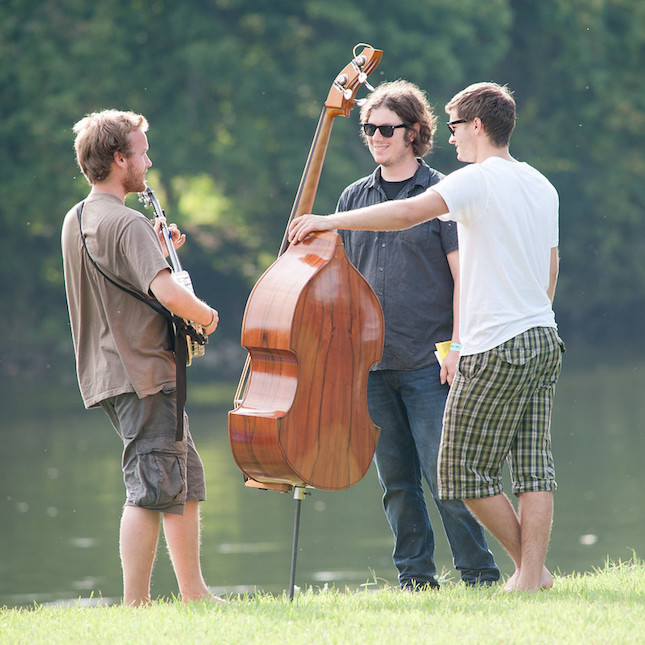 Bluegrass musicians stand in a circle by a river with smiles on their faces because everyone has practiced proper bluegrass jam etiquette