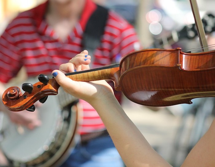 A fiddle plays in front of a banjo, both of which are traditional bluegrass instruments that don't violate bluegrass jam etiquette